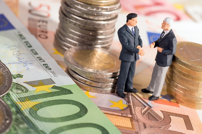 Foto: Zwei kleine Figuren stehend auf Geldscheine umringt von Münzen 